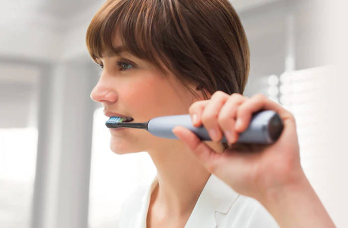 En kvinde b&oslash;rster t&aelig;nder med en gr&aring; Philips Sonicare.